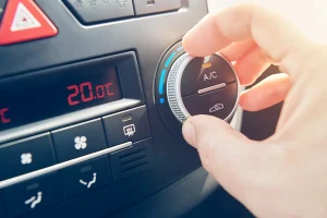 Closeup of car dashboard with a hand turning the air conditioning knob.