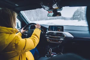 Woman driver wearing yellow coat driving through snowy woods